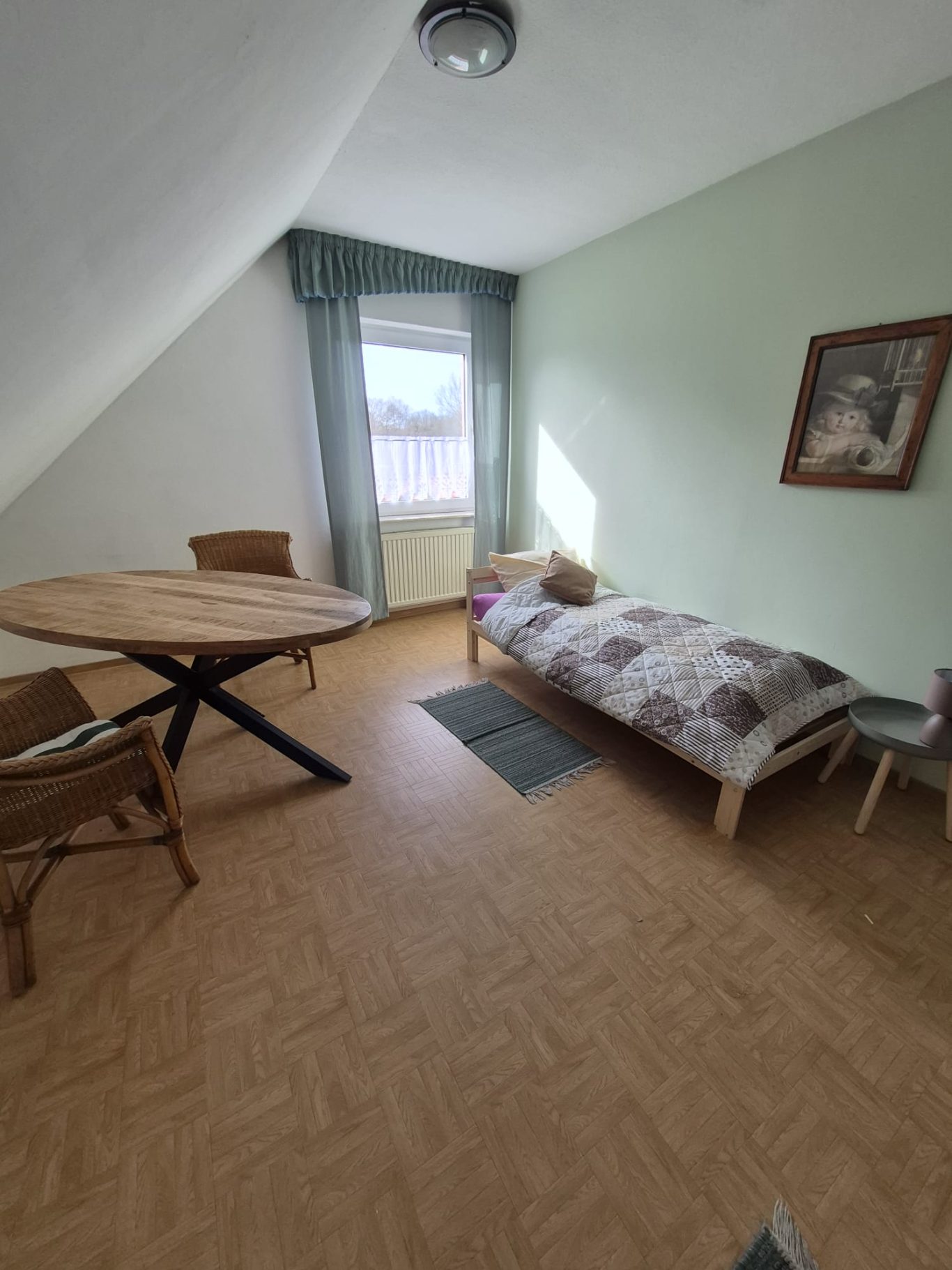 Ein heller Raum mit einem Bett, Tisch und Stühlen sowie einem Fenster und einem Bild an der Wand.