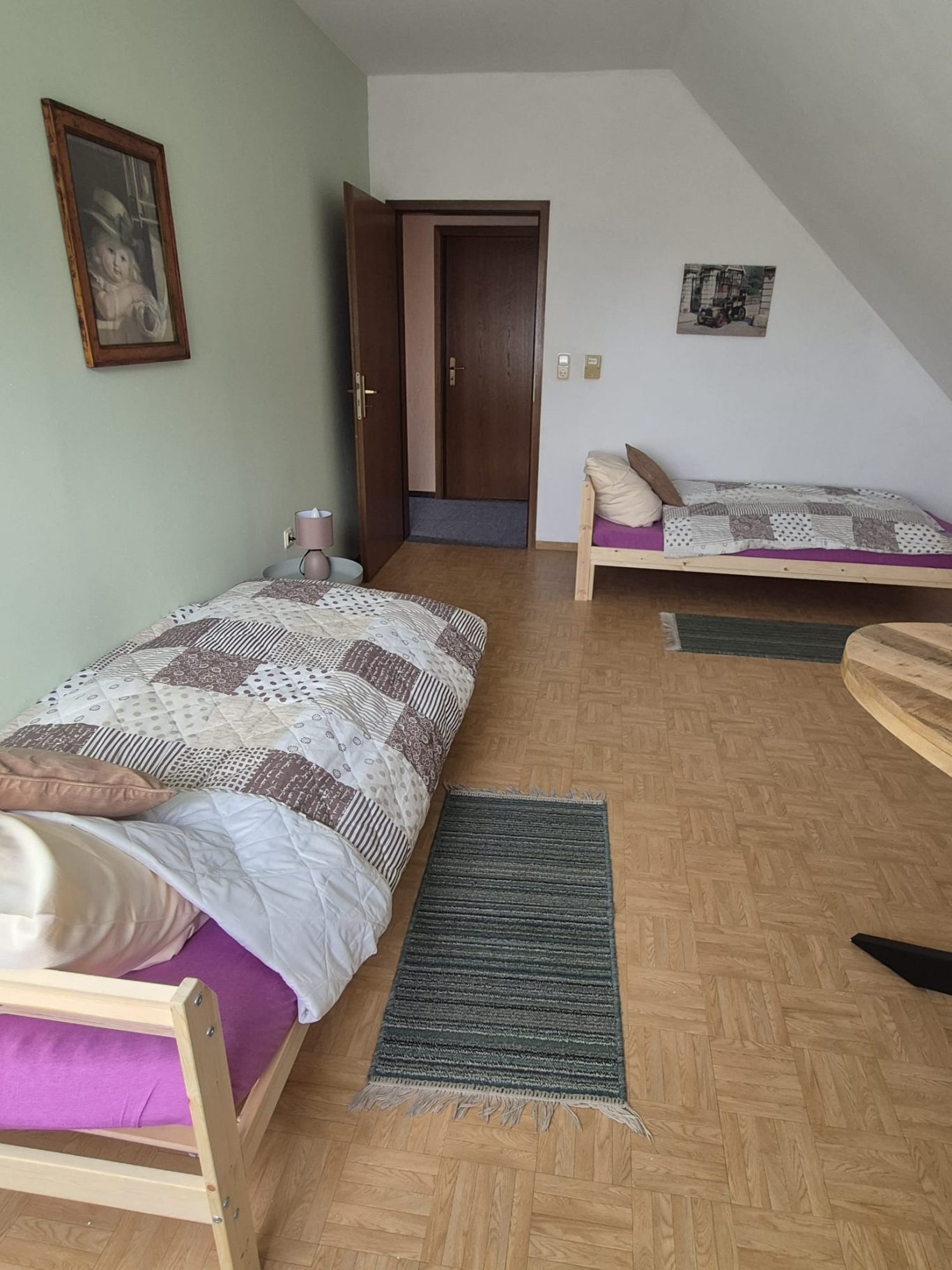 Ein einfaches Schlafzimmer mit zwei Betten, einem Tisch und einem Bild an der Wand.