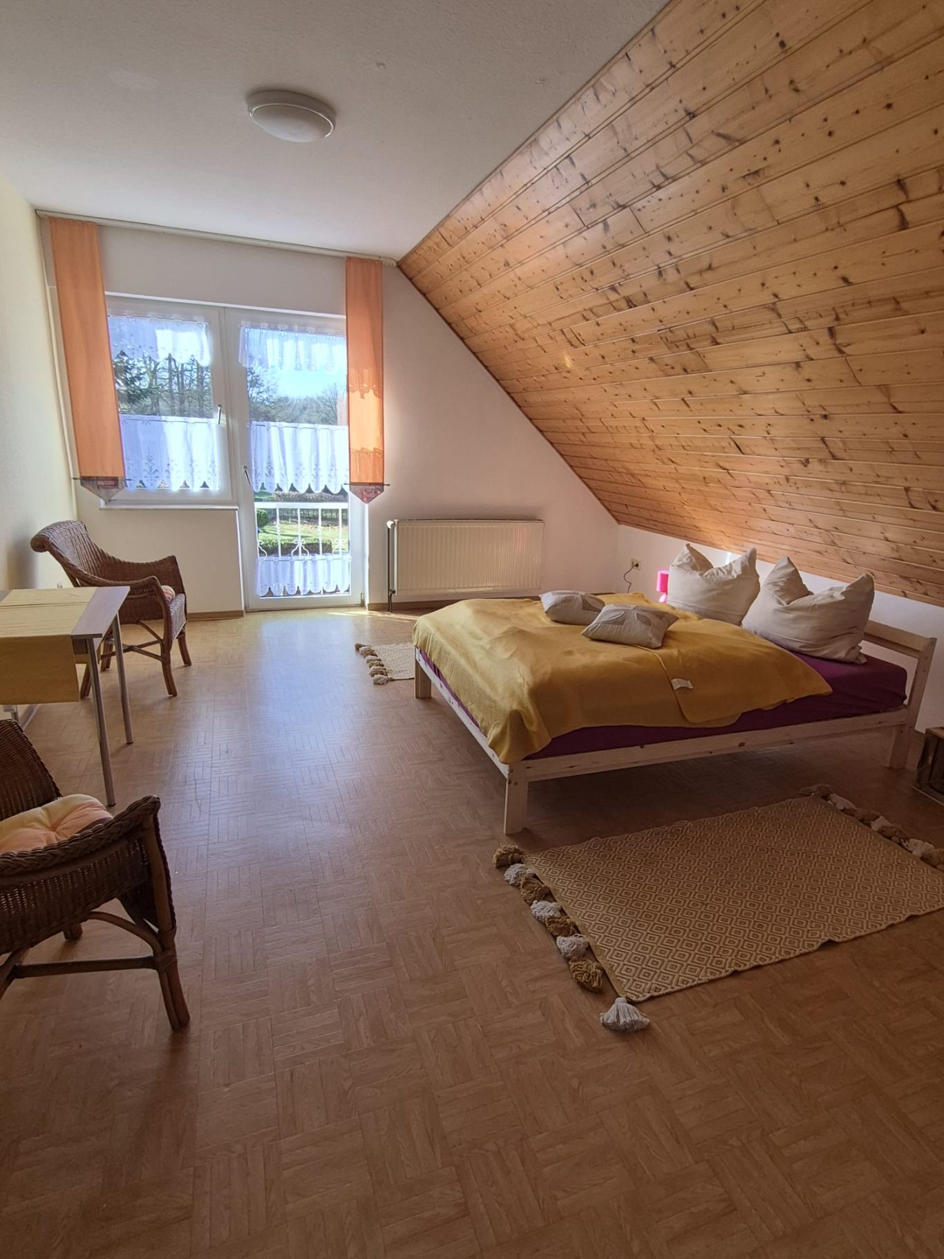 Helles Zimmer mit Holzdecke, zwei Betten, Tisch und Stühlen, Blick auf einen Garten.